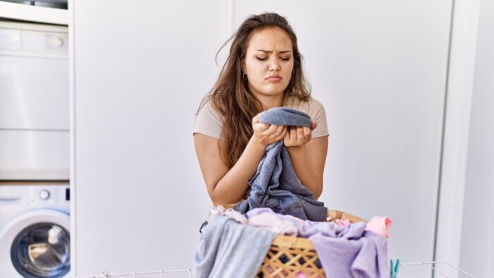 Mal olor en la ropa | Mujer oliendo ropa  desagradable. Canva Pro